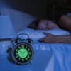Réveil à cloche sur une table basse devant une femme qui dort la nuit